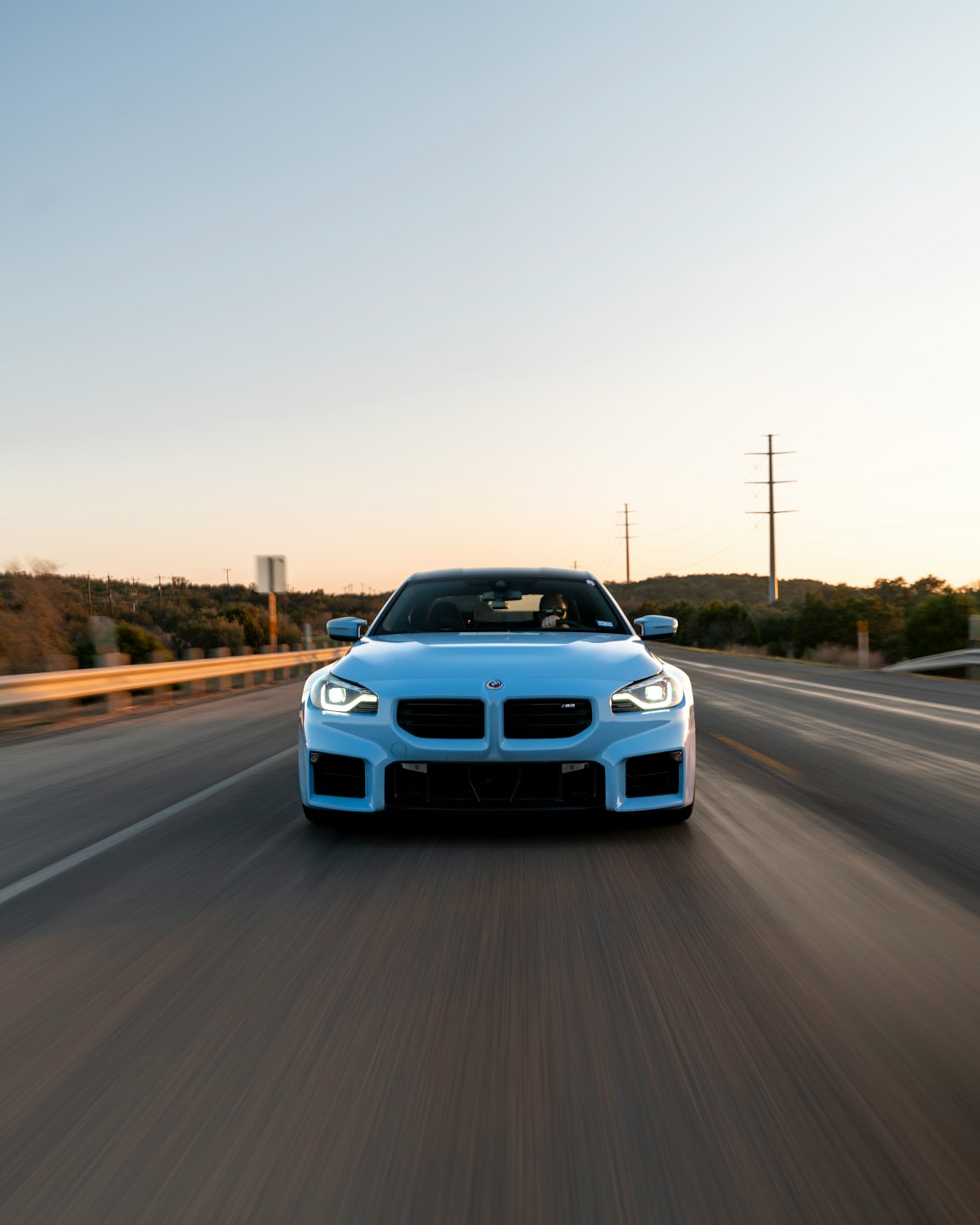 Light blue sports car speeding down a paved highway.