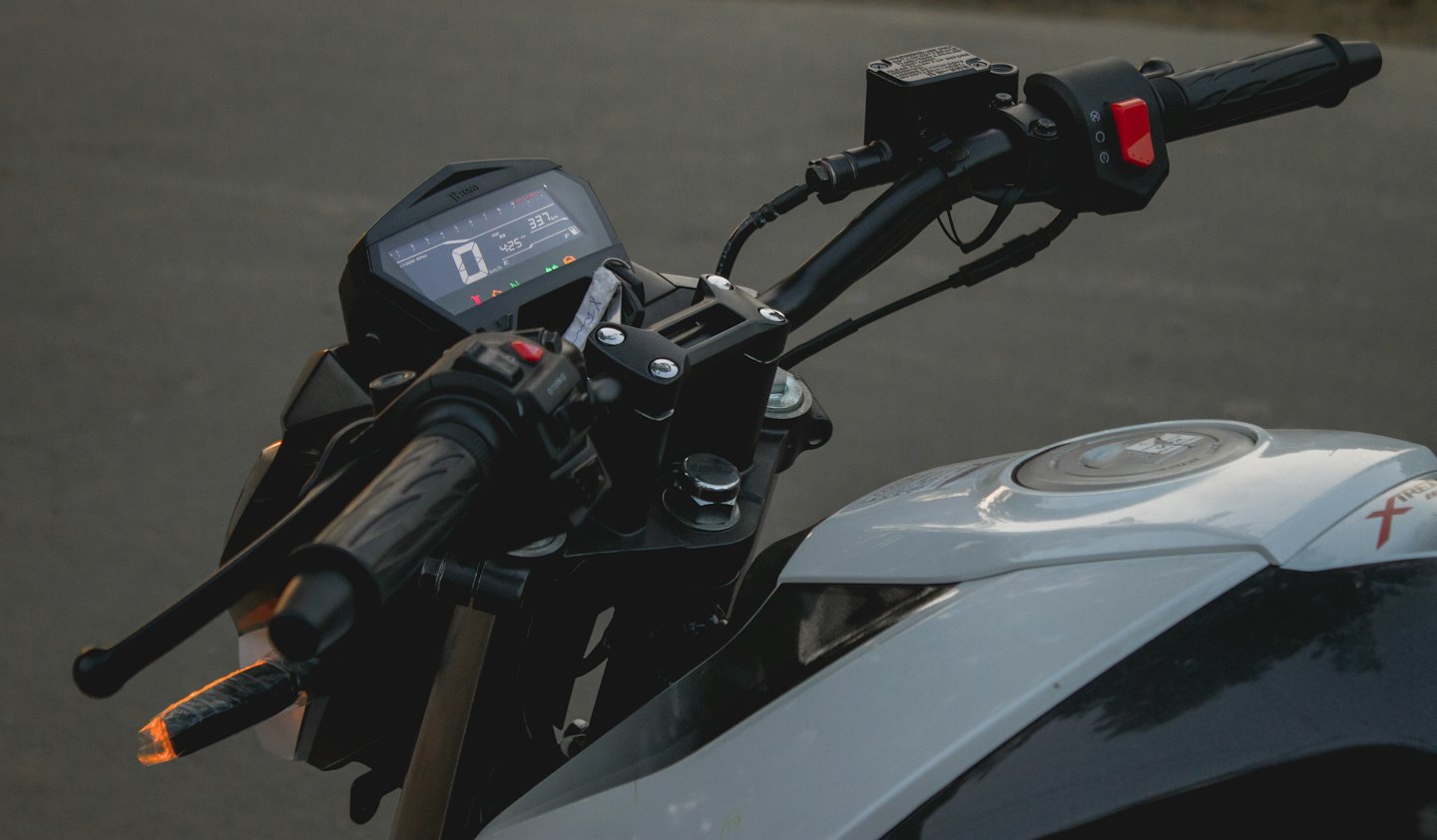Motorcycle handlebars with an illuminated digital dashboard and fuel tank.