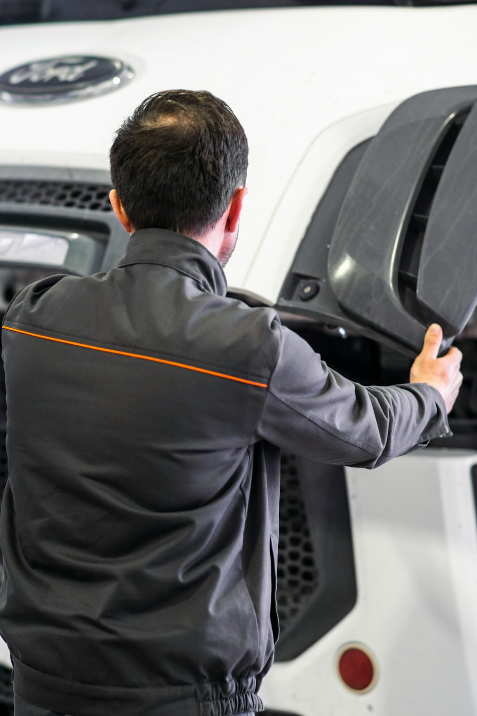 Mechanic inspects large vehicle engine bay holding a grey panel.