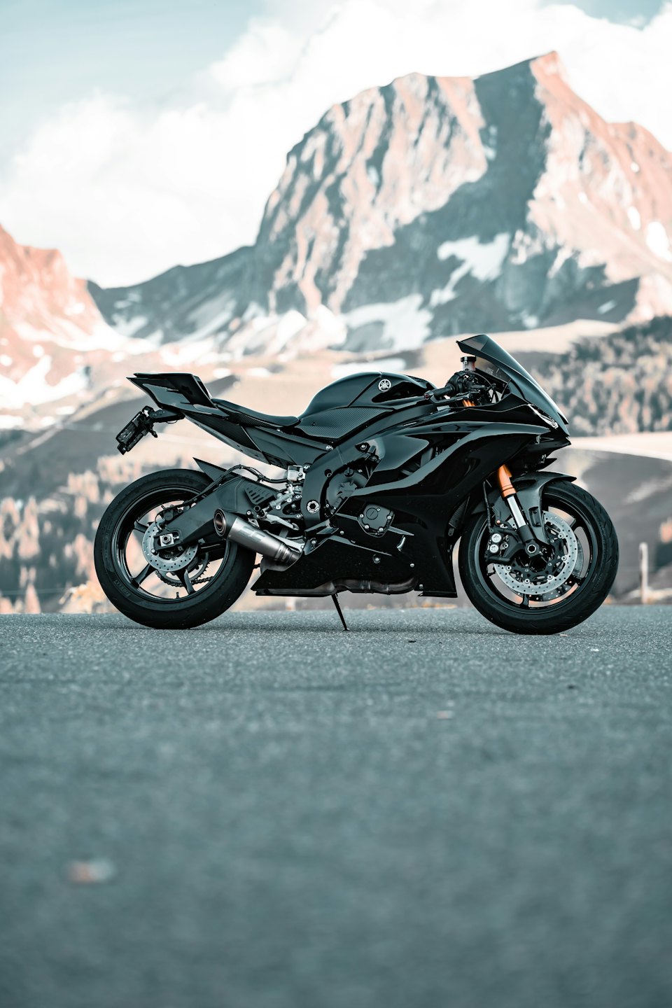 Black sport motorcycle parked on a road with snowy mountains.